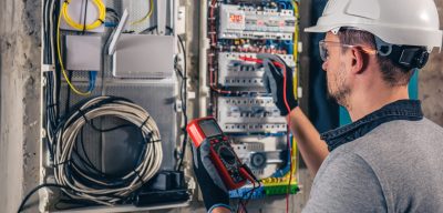 Man, an electrical technician working in a switchboard with fuses. Installation and connection of electrical equipment. Professional uses a tablet.